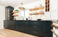 a large kitchen with wooden floors and green cabinetry, white walls and open shelving