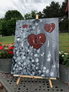 an easel with a painting on it that has hearts painted on it and flowers in the background