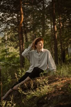 a woman is sitting in the woods with her head on her hand and looking up