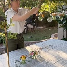 a woman is blowing bubbles on a table outside with flowers in the vases next to her