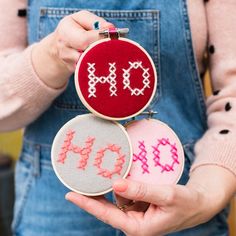 a woman holding three small embroidered cross stitched hoop frames with the word joy on them