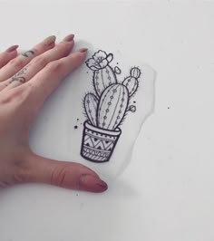 a woman's hand holding up a piece of paper with a drawing of a cactus in a pot