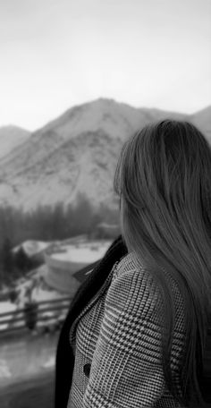 black and white photograph of a woman looking out at the snow covered mountains behind her