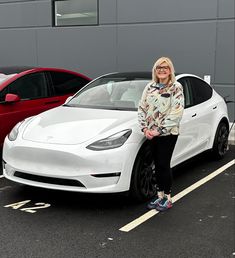 a woman standing next to a white car in a parking lot