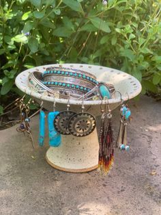 a white bowl filled with jewelry sitting on top of a cement ground next to plants