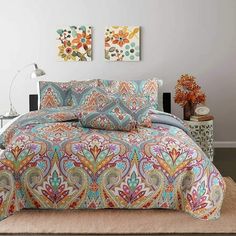 a bed covered in a colorful comforter next to a lamp and painting on the wall