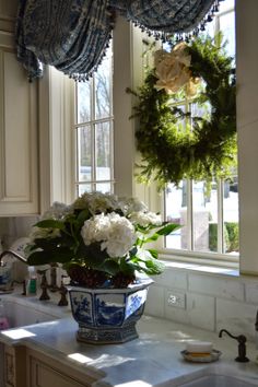 white flowers in a blue and white bowl on a kitchen counter next to a window