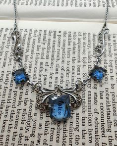 Gorgeous vintage Art Deco necklace with open back blue glass set in chrome filigree. The blue glass is a vibrant sapphire colour and the setting reminds me of a butterfly, which I think is uniquely lovely. There is also a mark on the clasp ring but I can't make it out. In very good vintage condition with some wear to the chrome finish (please see photos), and could use a thorough clean by someone who knows what they're doing. The necklace is 41cm long and the centre stone measures 1.1cm by 0.9cm Antique Blue Metal Jewelry, Antique Blue Gemstone Necklaces, Victorian Blue Necklaces For Formal Occasions, Blue Victorian Necklace For Formal Occasions, Victorian Style Blue Necklaces For Formal Occasions, Art Deco Blue Pendant Necklace, Vintage Blue Pendant Necklace, Blue Victorian Metal Jewelry, Vintage Sapphire Jewelry For Collectors