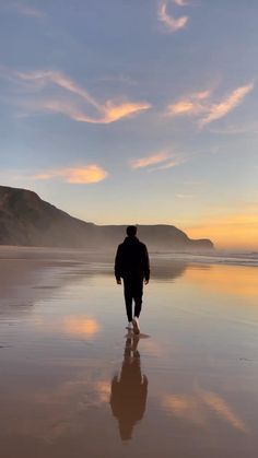 a man walking on the beach at sunset with his back turned to the camera as he walks towards the water