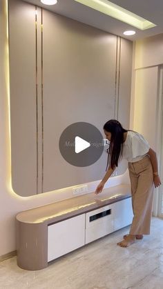 a woman standing in front of a tv on top of a white cabinet next to a window