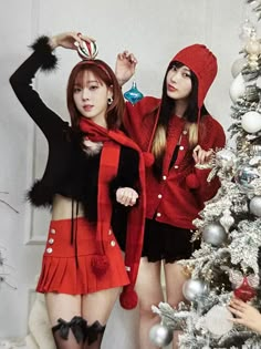 two women in red and black outfits standing next to a christmas tree