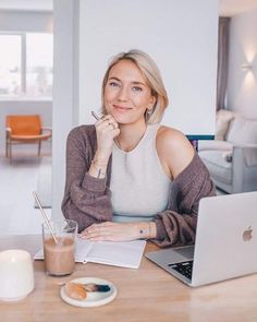 a woman sitting at a table in front of a laptop computer and holding a pen