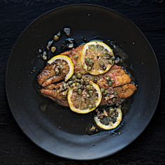 fish with lemons and capers on a black plate