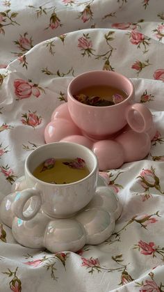 a cup of tea and saucer sitting on a floral bed sheet with pink roses