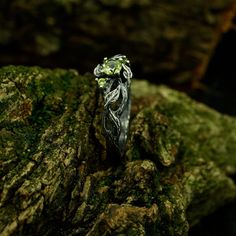 a wedding ring sitting on top of a rock covered in green mossy leaves and stones