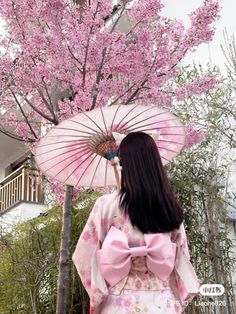 a woman standing in front of a tree with pink flowers and an umbrella over her head