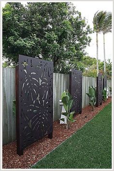 a fence that is next to some plants in the grass and trees on the other side