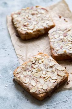 three pieces of bread topped with almonds on top of a piece of parchment paper