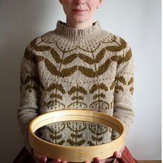 a woman is holding a round object in her hands and wearing a knitted sweater