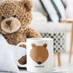 a brown teddy bear sitting next to a white coffee mug with the word harper on it