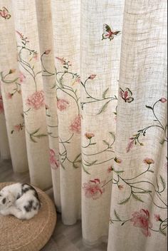 a cat laying on top of a rug next to a window covered in curtains with flowers