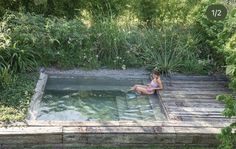 a woman sitting in the middle of a pool surrounded by trees and plants on either side