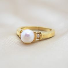 This classic pairing features a white Akoya pearl set in 14K yelloow gold with a diamond on either side of the pearl setting. Akoya pearls are luxurious pearls found in the Japan and China regions. They are renowned for their brilliant luster and their perfect roundness. ADDITIONAL INFORMATION: Pearl Size: approx.7.3 diameter freshwater pearls Diamonds: .05TW round diamonds Clasp Material: 14K Yellow Gold Band Width: 2.2mm Ring Size: Current size 7 *During the sale, ring sizing is not included. Pearl Setting, Akoya Pearl Ring, Pearl Set, Akoya Pearls, Pearl Diamond, Pearl Size, Custom Engagement Ring, The Pearl, Pearl Ring