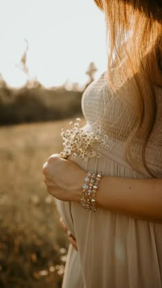 a woman in a white dress is holding her hand on her chest and wearing a bracelet with pearls