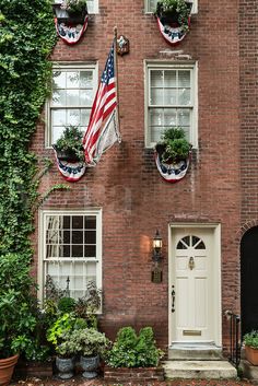 an american flag hanging on the side of a brick building with potted plants in front