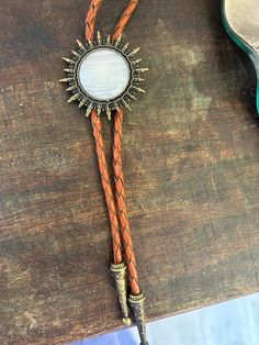 This awesome bolo tie has a southwestern brass sun design and pearl white stone centerpiece. The cord is brown genuine leather. Our bolos pair nicely with many of our belt buckles! They make wonderful gifts. The western bolo tie rope length is 39'' ; charm pendant size is 1 1/2'' Vintage Bolo Ties With Adjustable Length For Western-themed Events, Vintage Bolo Tie With Adjustable Length For Western Events, Adjustable Gold Western Bolo Ties, Vintage Brown Jewelry With Adjustable Length, Lariat Bolo Tie With Adjustable Length For Western-themed Events, Adjustable Vintage Bolo Ties For Ranch, Gold Western Bolo Tie, Vintage Bolo Ties With Adjustable Length For Rodeo, Adjustable Brown Western Jewelry