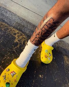 a man wearing yellow clogs with tattoos on his legs