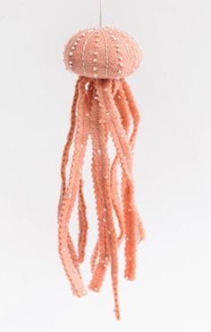 a pink jellyfish ornament hanging from a white ceiling with beads on it