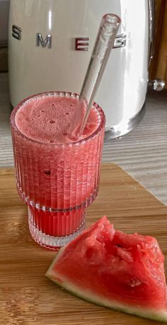 a watermelon drink in a glass next to a slice of watermelon