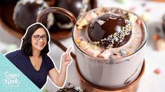 a woman holding up a spoon next to a cup filled with chocolate and sprinkles