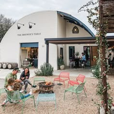 people sitting around a fire pit in front of a building with barrels on the outside