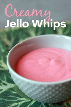 a white bowl filled with pink jello on top of a green leafy surface