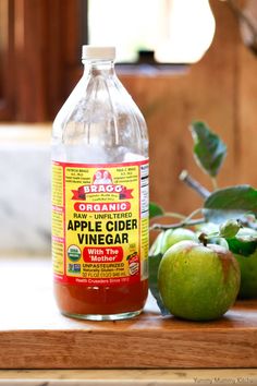 two bottles of apple cider vinegar sit on a counter next to apples and leaves