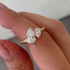 a woman's hand with a diamond ring on top of her finger, showing the two pear shaped diamonds