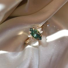 a green ring sitting on top of a white satin covered table cloth with an emerald colored stone in the center