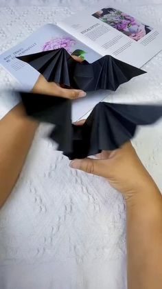 two hands holding black folded paper in front of an open book with pictures on it