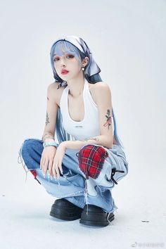 a woman with blue hair sitting on the ground wearing jeans and a white tank top