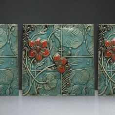 three pieces of art with red flowers on green tiles in front of a black wall