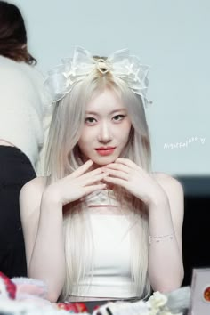 a woman with long white hair and a bow on her head sitting at a table