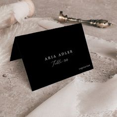 a close up of a black business card on a white table cloth with an object in the background