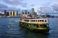 a green and white boat in the water with city buildings in the backgroud