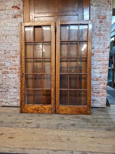 two wooden doors sitting next to each other in front of a brick wall and floor