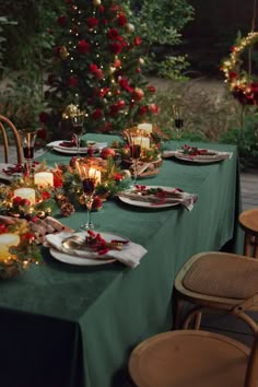 a table set for christmas dinner with candles, plates and decorations in front of a tree