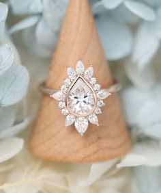 an engagement ring with a pear shaped diamond surrounded by blue and white flowers in the background