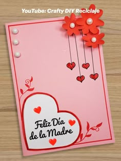 a pink card with red flowers and hearts on it, that says feliz dia de la madre