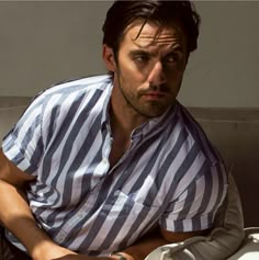 a man sitting on top of a couch next to a white wall and wearing a watch